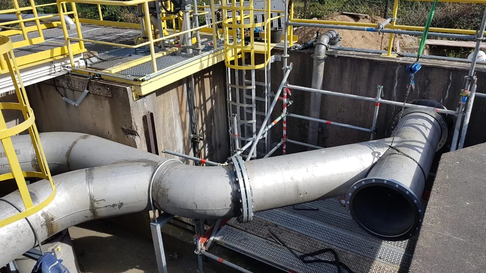 Große Rohrleitungen mit Bögen, Flanschen und gelben Geländern in einer Industrieanlage